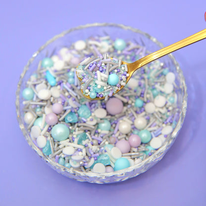 Pastel blue and purple sprinkles on a spoon over a bowl with a purple background
