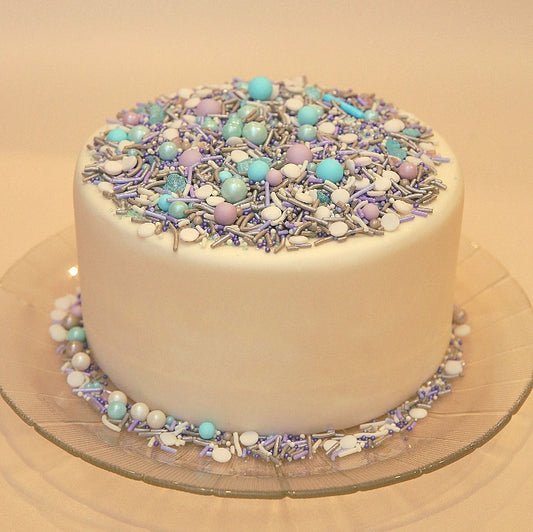 White cake with colorful sprinkles on a clear cake stand.
