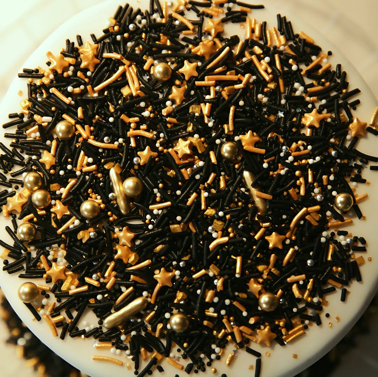 Assorted black, gold, and gold star-shaped sprinkles on a white cake.