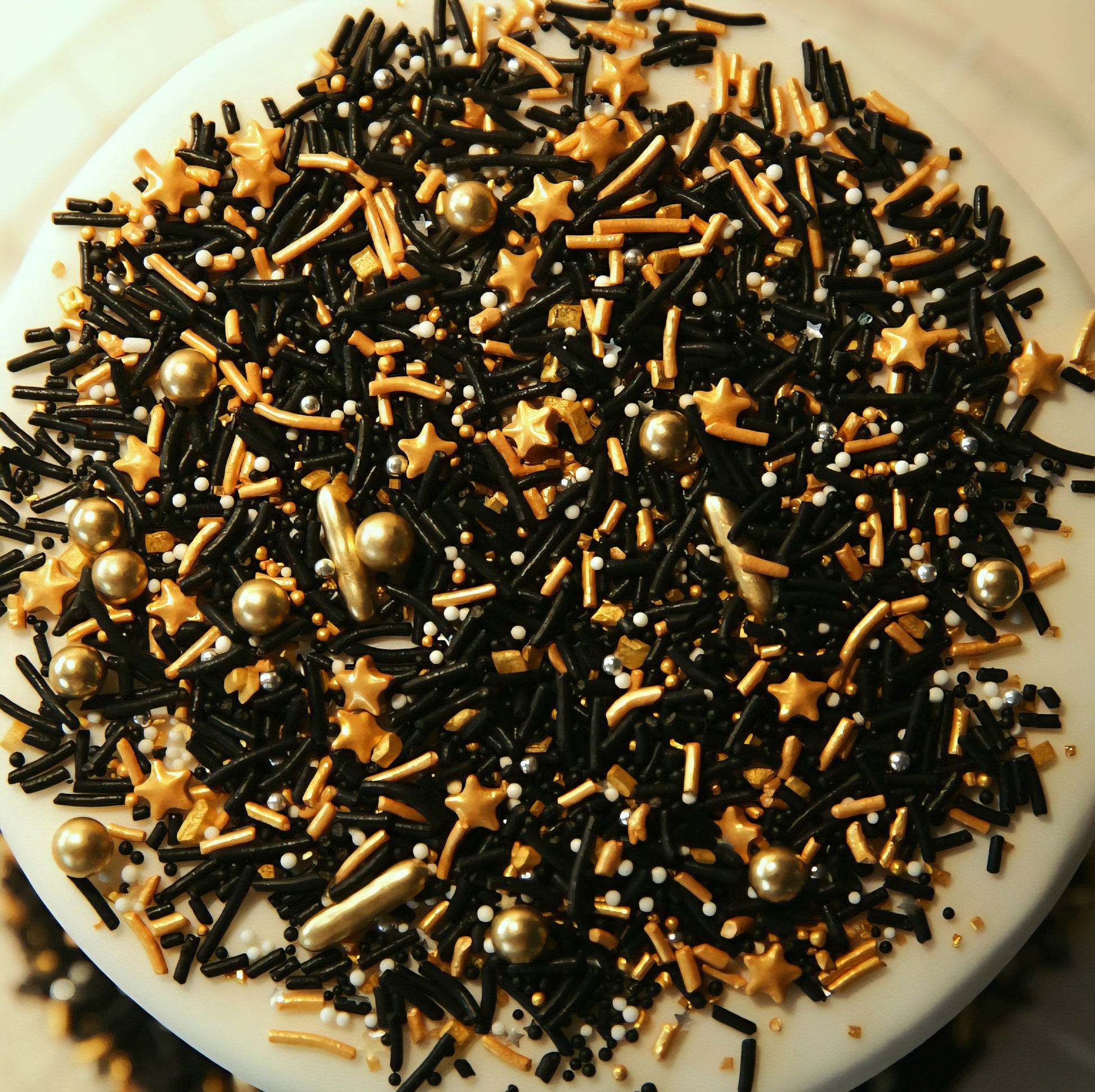 Assorted black, gold, and gold star-shaped sprinkles on a white cake.