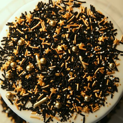 Assorted black, gold, and gold star-shaped sprinkles on a white cake.