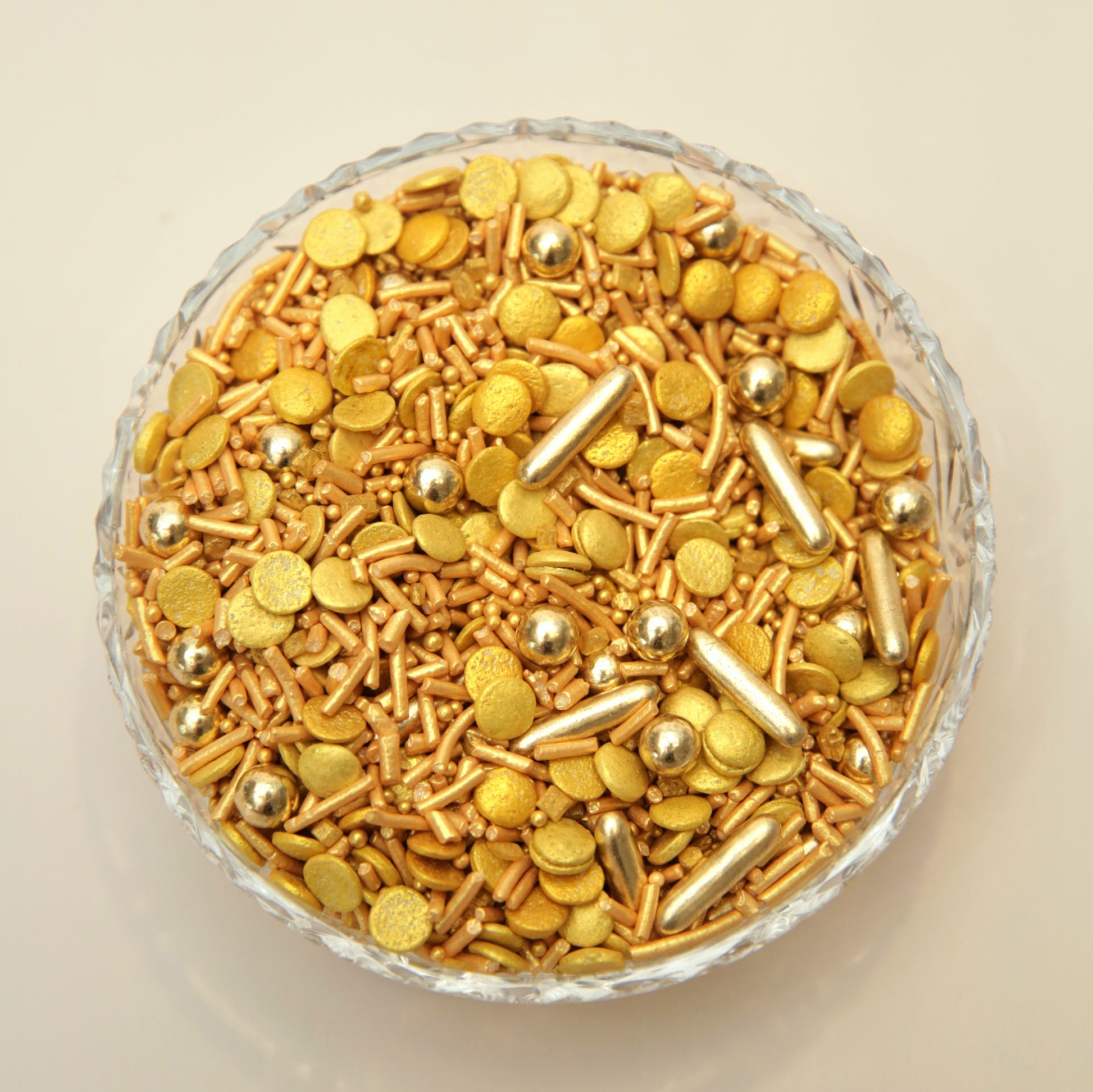 Assorted gold sprinkles in a glass bowl on a beige background