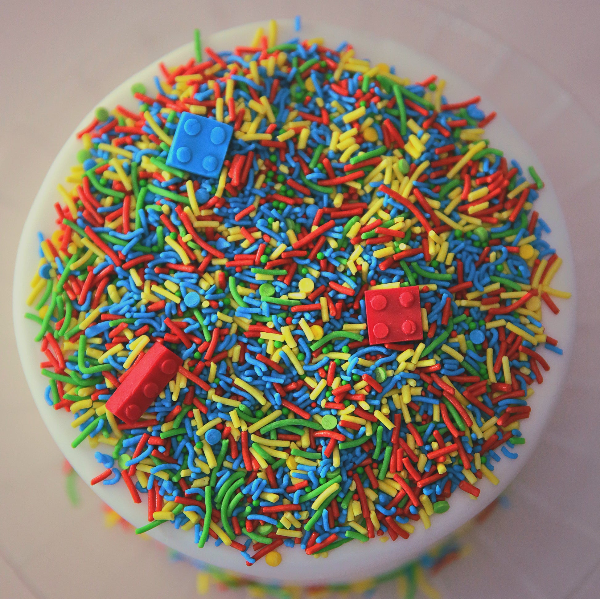 Colourful sprinkles with edible bricks on a white cake