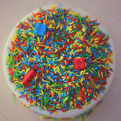 Colourful sprinkles with edible bricks on a white cake