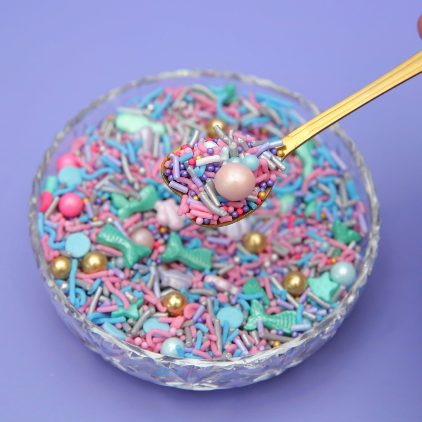 Mermaid inspired sprinkles with a gold spoon on a purple background