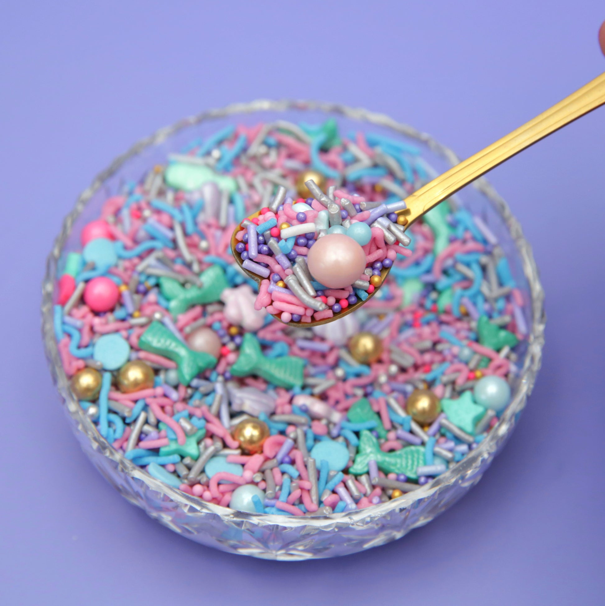 Mermaid inspired sprinkles with a gold spoon on a purple background