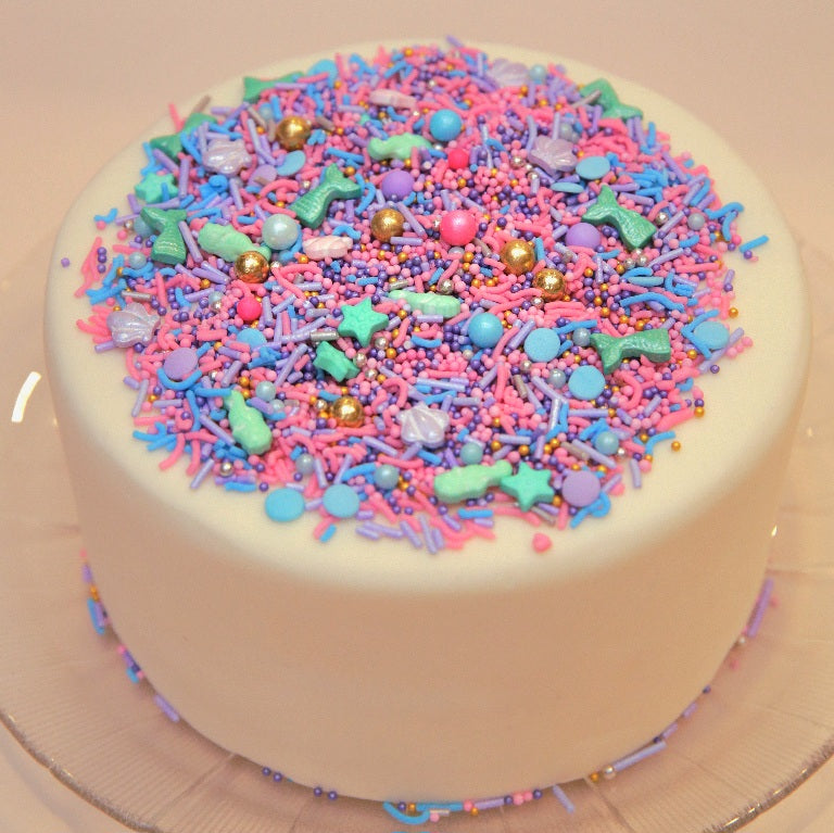 White cake with colorful Mermaid sprinkles on a beige background