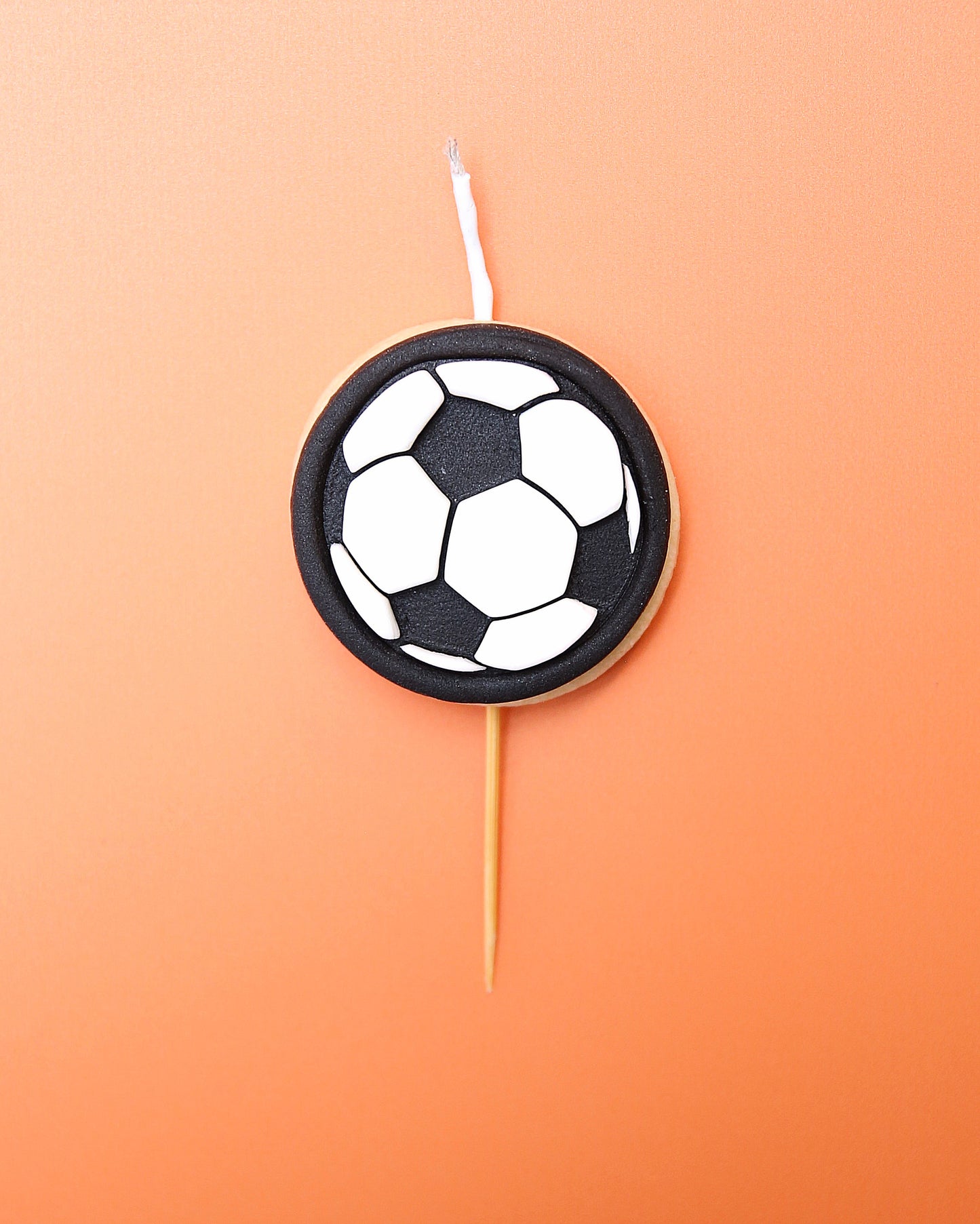 A Mini soccer ball cookie candle on an orange background 