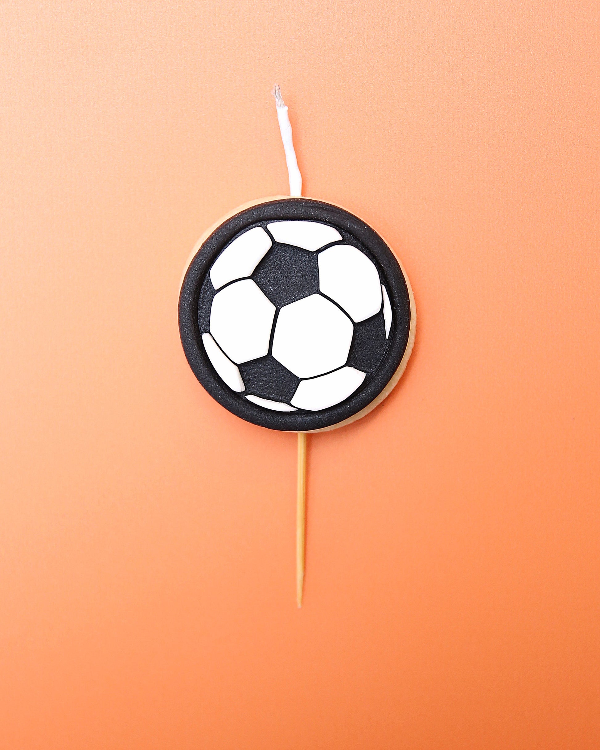 A Mini soccer ball cookie candle on an orange background 