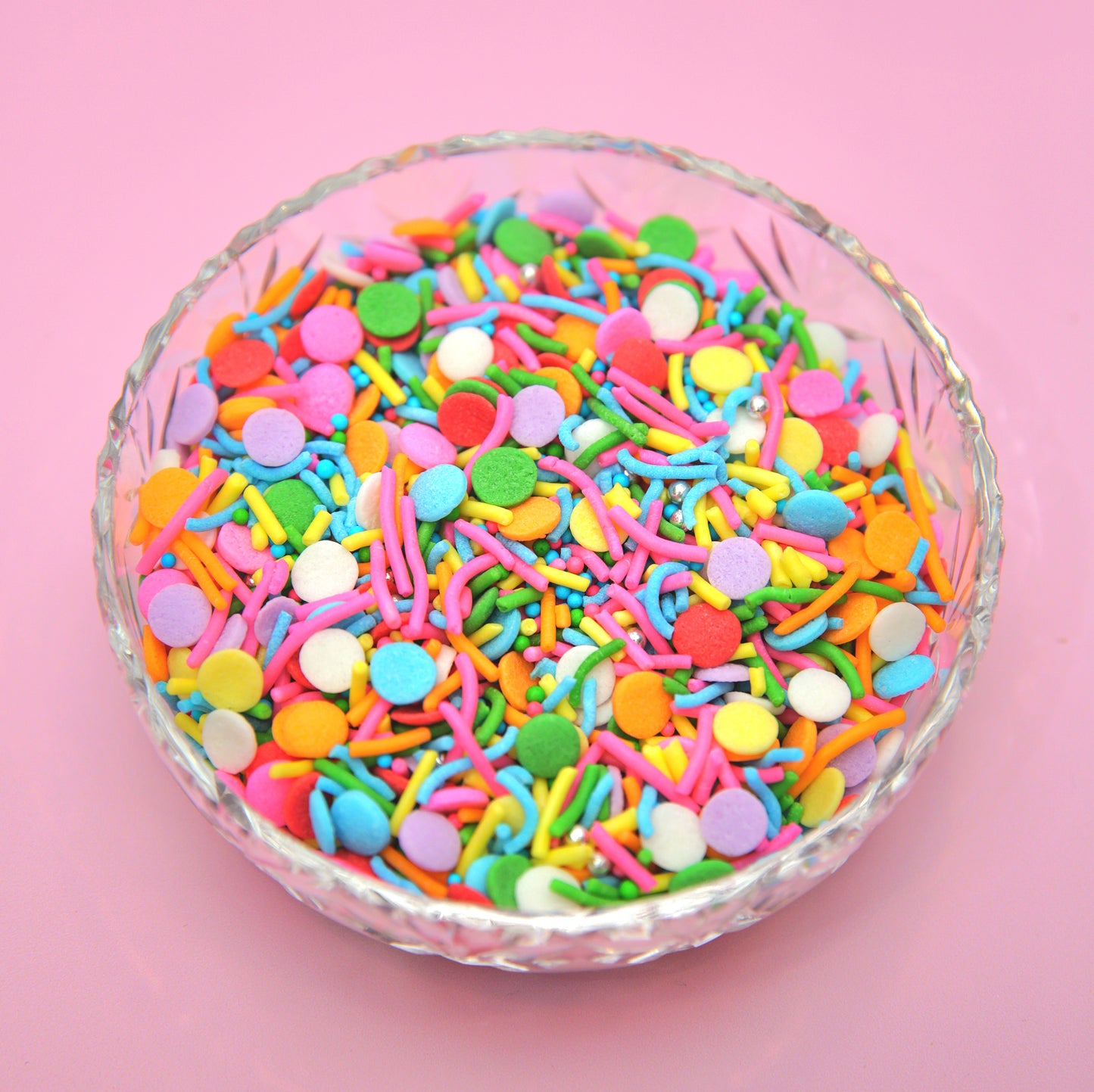 Glass bowl filled with colorful sprinkles on a pink background
