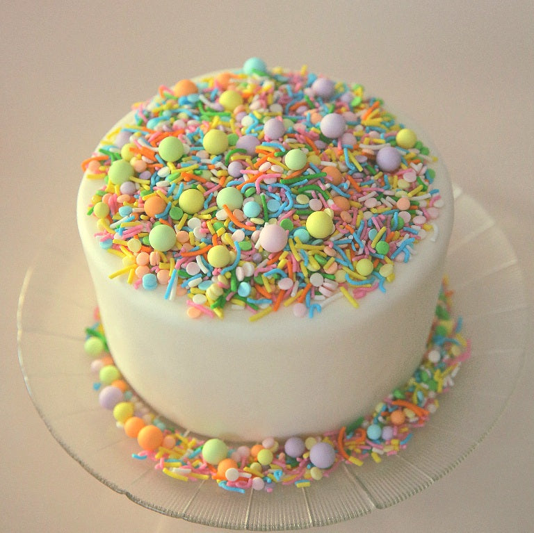 White cake with pastel rainbow sprinkles on a beige background