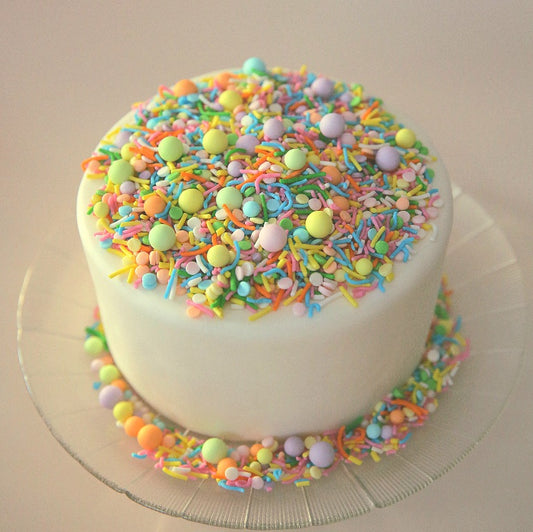 White cake with pastel rainbow sprinkles on a beige background