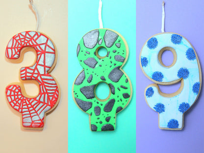 Three decorative cookies shaped like numbers 3, 8, and 9 on a beige, blue, and purple background.