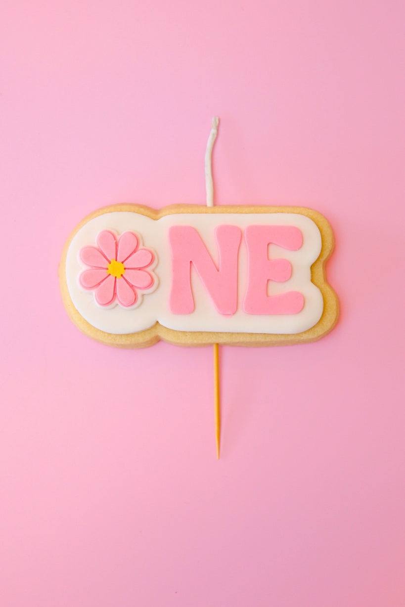 Candle shaped like the number 'ONE' with a flower on a pink background