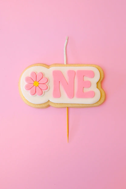Candle shaped like the number 'ONE' with a flower on a pink background