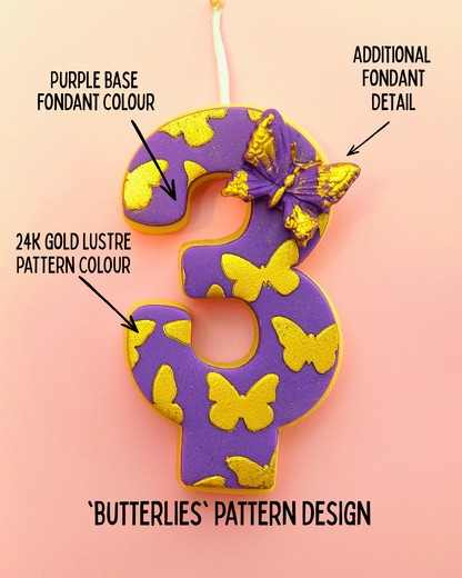 Decorative number '3' edible birthday candle with purple base, gold lustre, and butterfly pattern on a pink background.