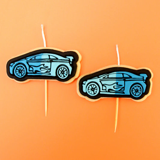 Two car-shaped candle cookies on toothpicks against an orange background