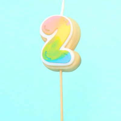 Colorful number 2 cake candle on a stick against a light blue background