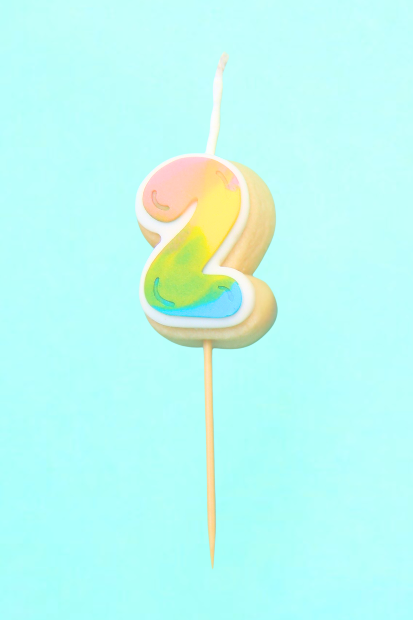 Colorful number 2 cake candle on a stick against a light blue background