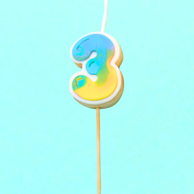 Colorful number 3 cookie on a stick against a light blue background