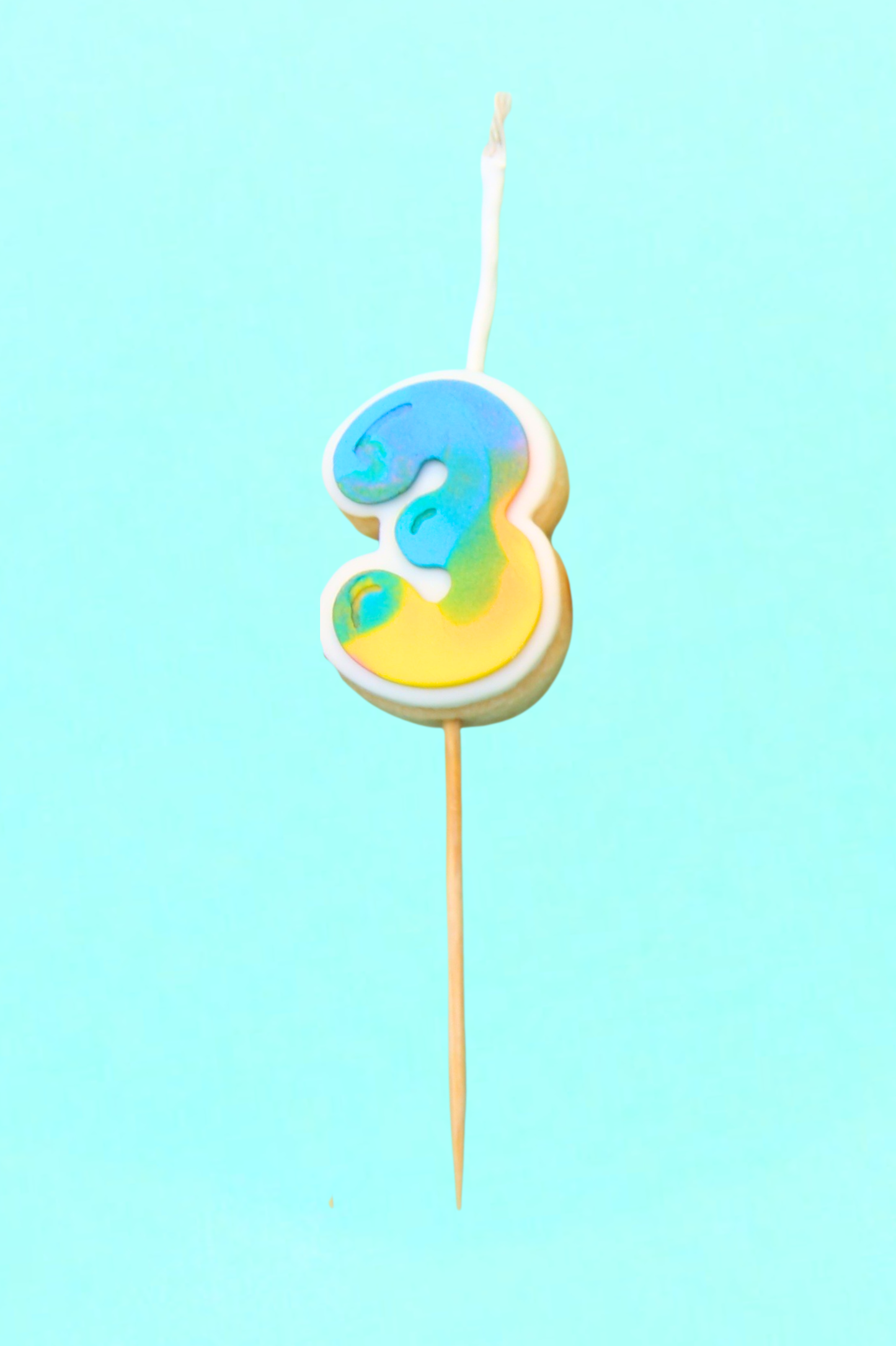 Colorful number 3 cookie on a stick against a light blue background
