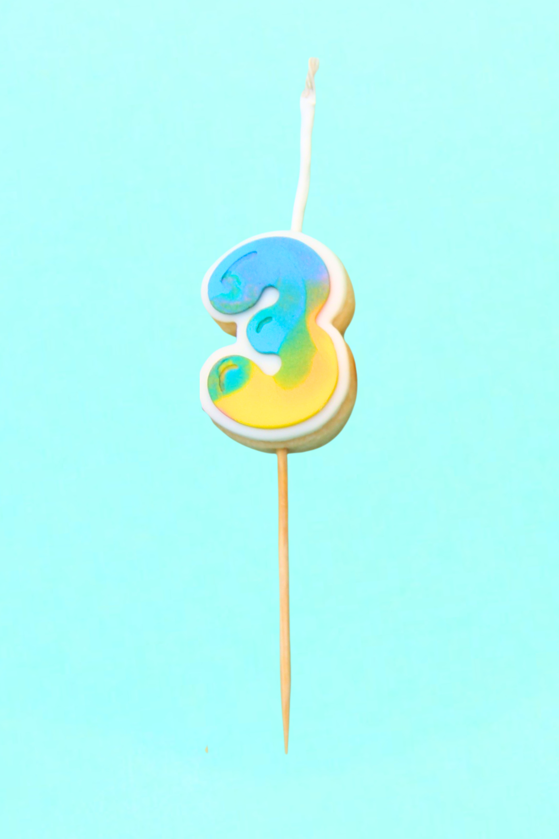 Colorful number 3 cookie on a stick against a light blue background