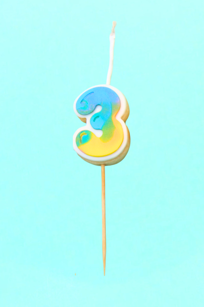 Colorful number 3 cookie on a stick against a light blue background