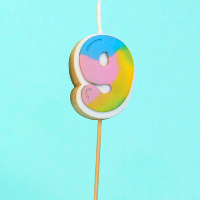 Colorful 9 shaped cookie candle on a stick against a light blue background