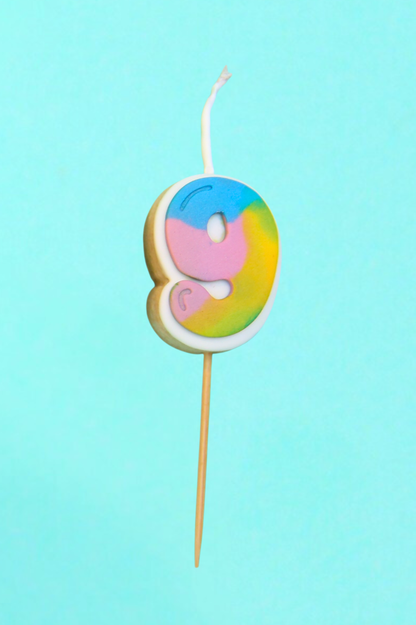 Colorful 9 shaped cookie candle on a stick against a light blue background
