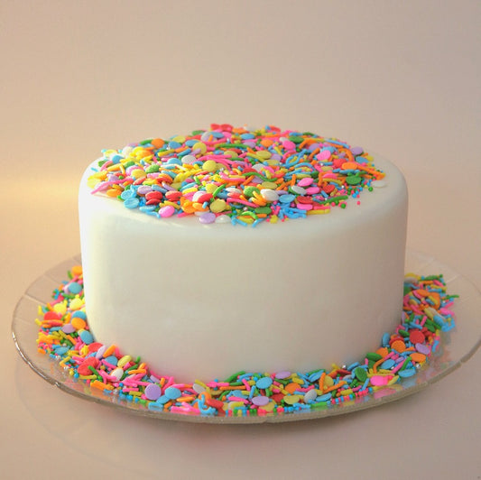 White cake with colorful sprinkles on a clear plate against a beige background