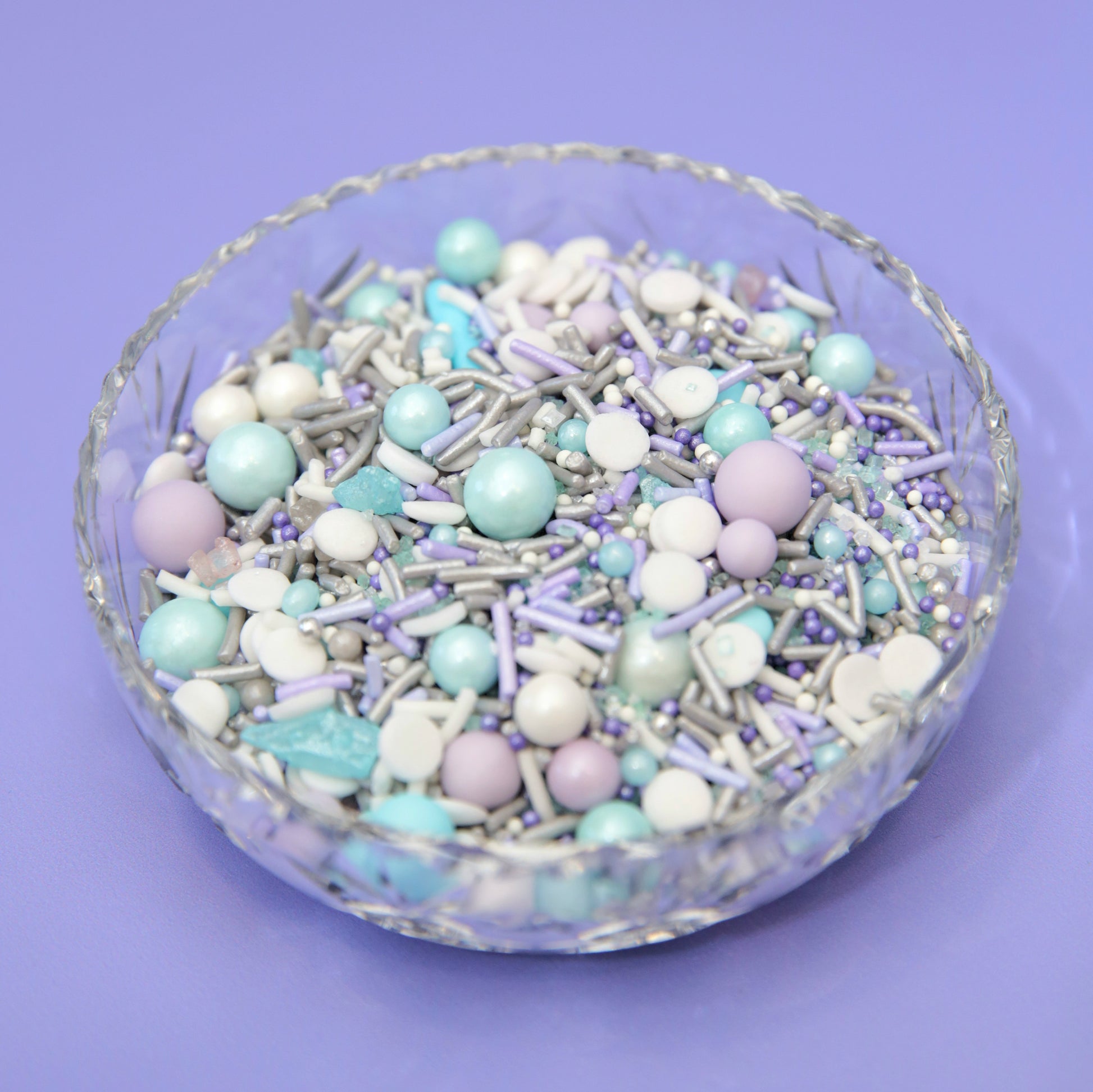Glass bowl filled with pastel purple and blue sprinkles on a purple background