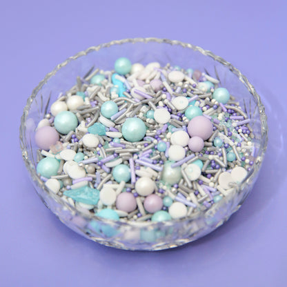 Glass bowl filled with pastel purple and blue sprinkles on a purple background