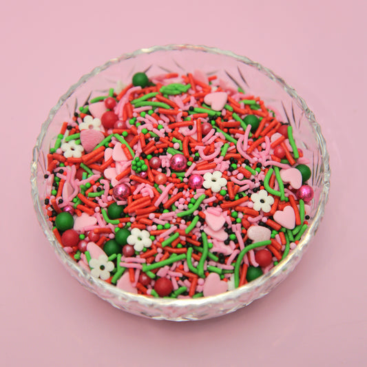 Glass bowl filled with pink, red and green sprinkles on a pink background