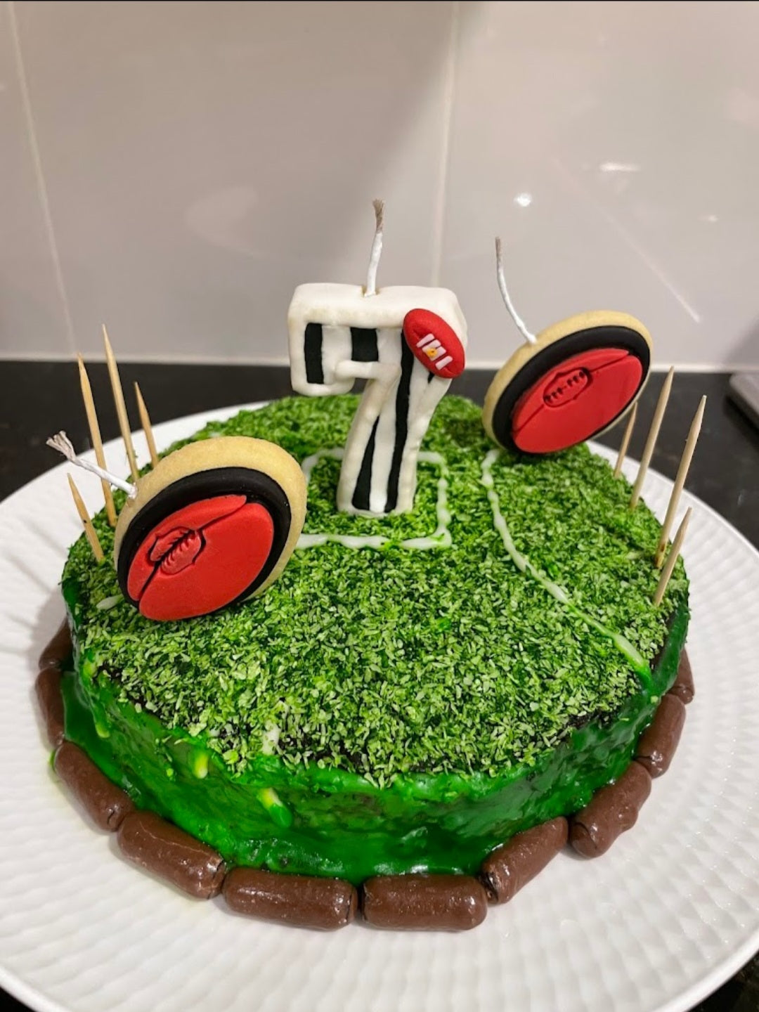 A number seven Collingwood themed cookie candle with AFL football mini cookie candles on an AFL themed cake