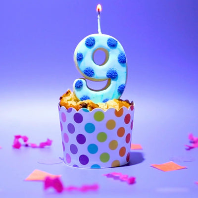 A blue spotty number nine Cookie Candle on a cupcake with colourful confetti 