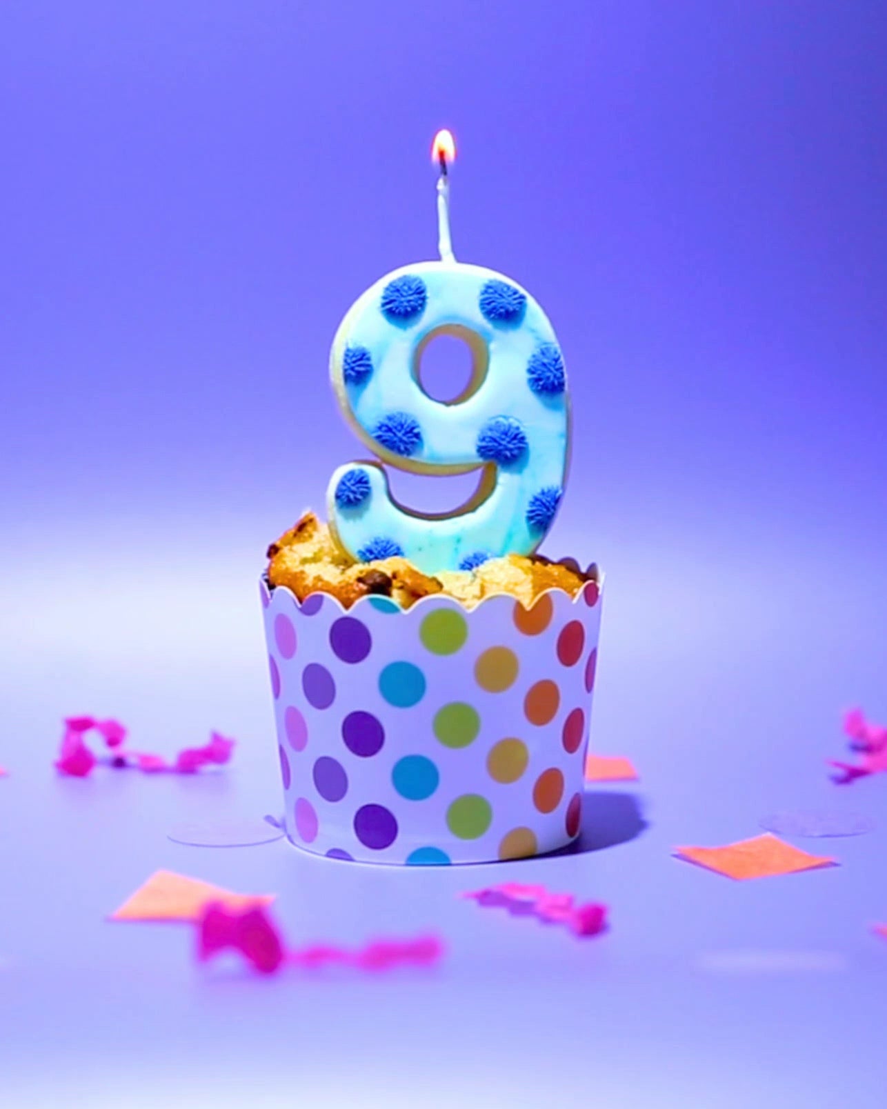 A blue spotty number nine Cookie Candle on a cupcake with colourful confetti 