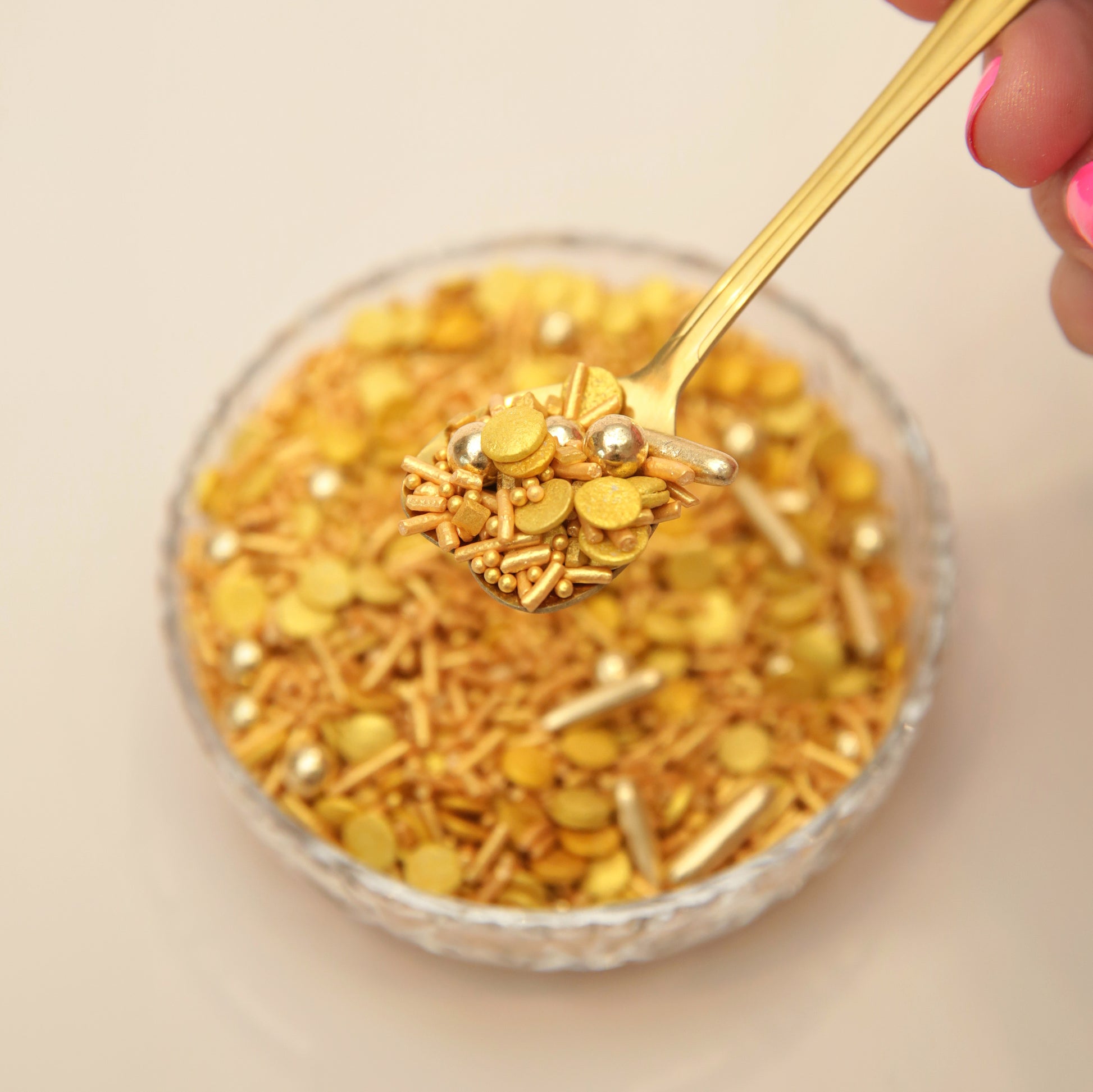 Gold sprinkle mixture on a spoon over a bowl on a beige background