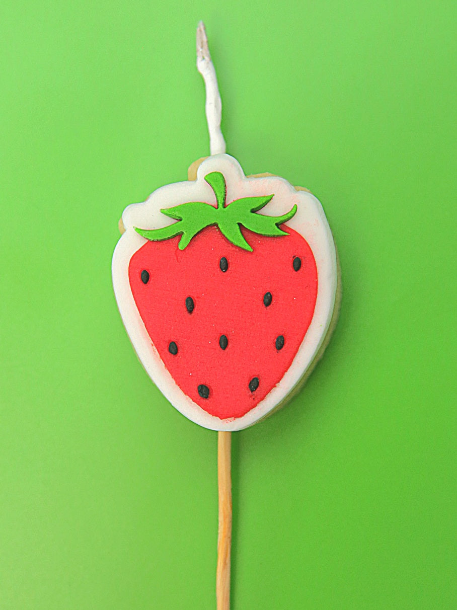Strawberry-shaped cookie cake topper and candle on a green background