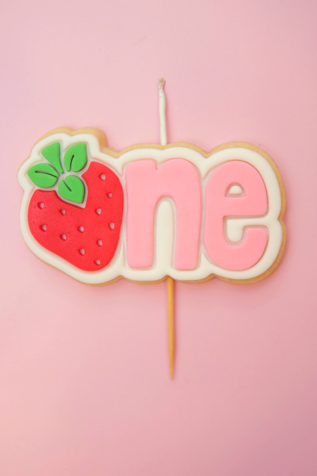 Decorative cake topper with strawberry and 'one' on a pink background