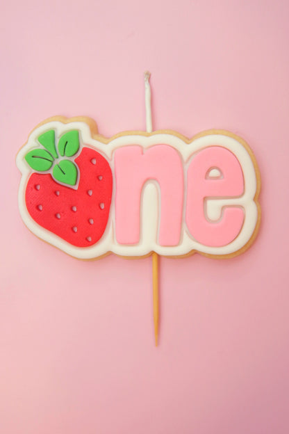 Decorative cake topper with strawberry and 'one' on a pink background