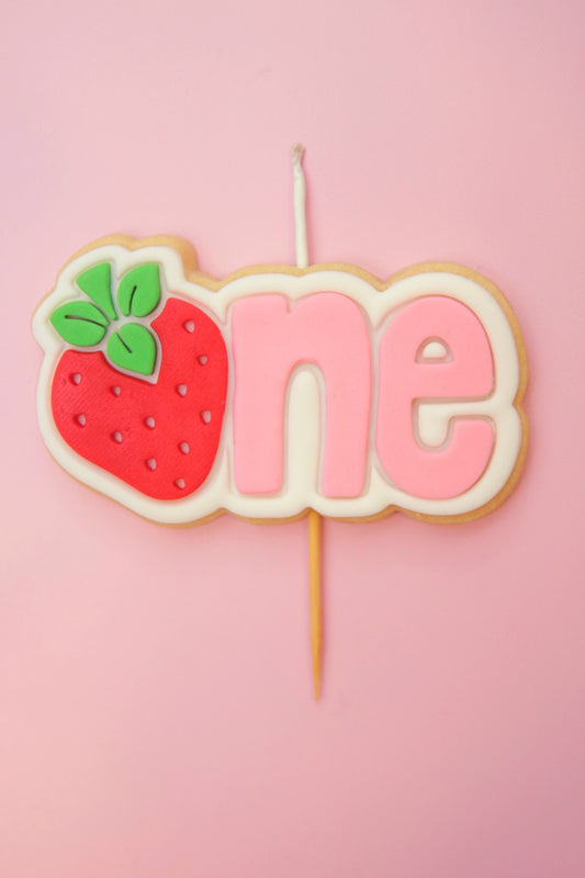 Decorative cake topper with strawberry and 'one' on a pink background