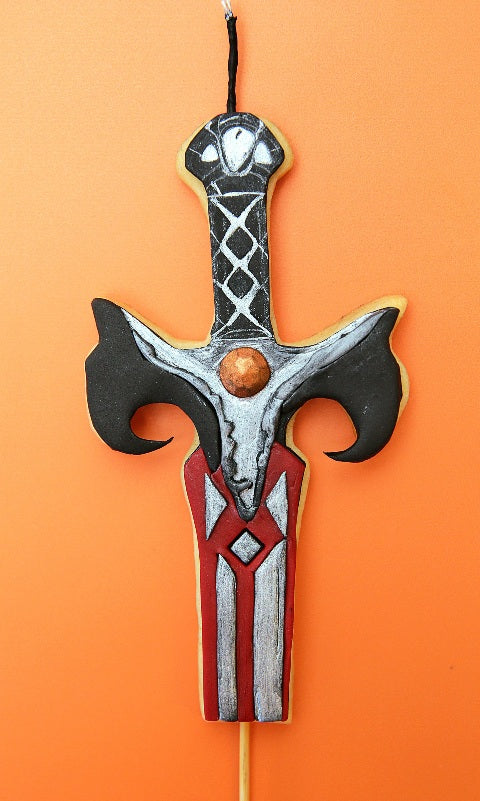 A cookie candle cake topper shaped and decorated like a mediaeval sword with a black lightable wick. 
