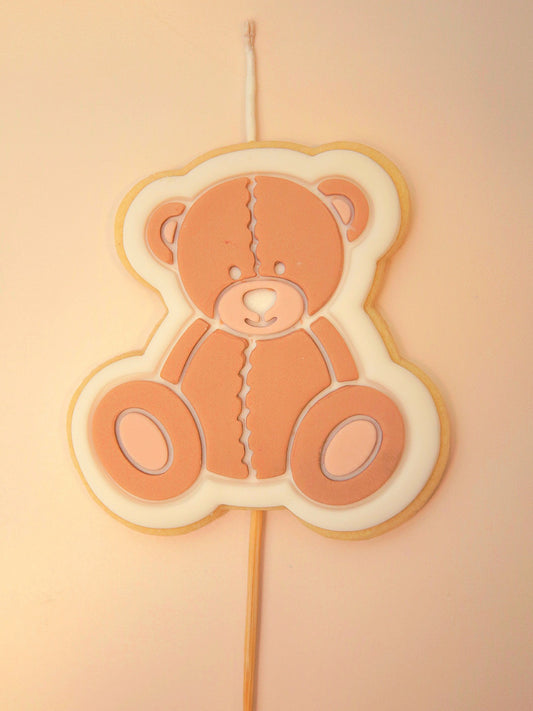 Teddy bear-shaped cookie on a stick with a wick against a beige background