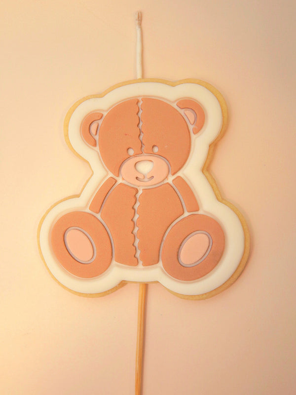 Teddy bear-shaped cookie on a stick with a wick against a beige background