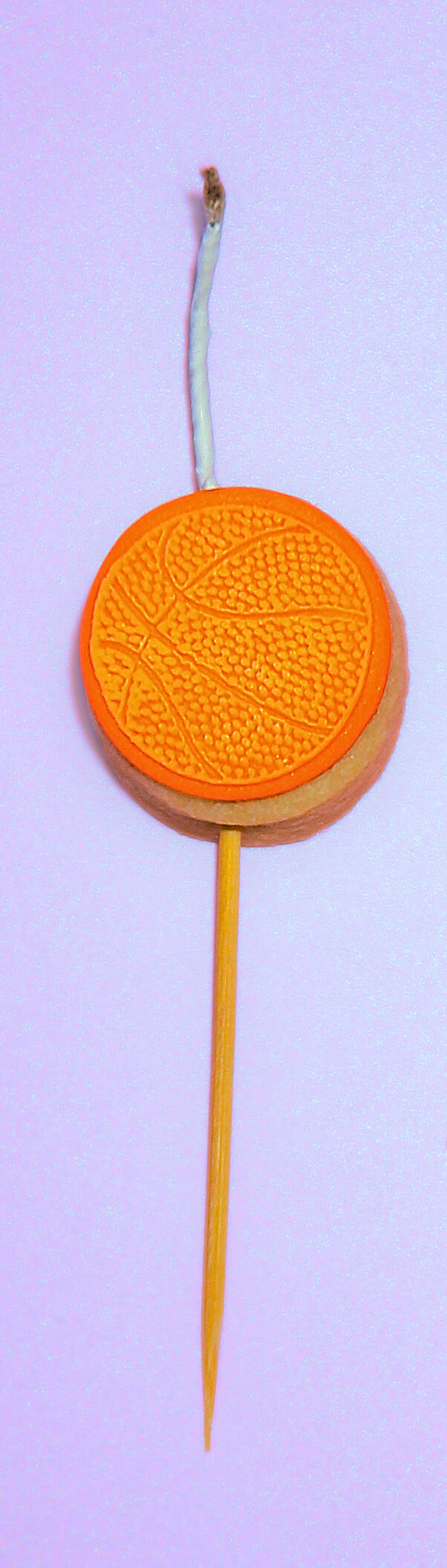 Orange basketball cookie candle on a wooden stick against a purple background
