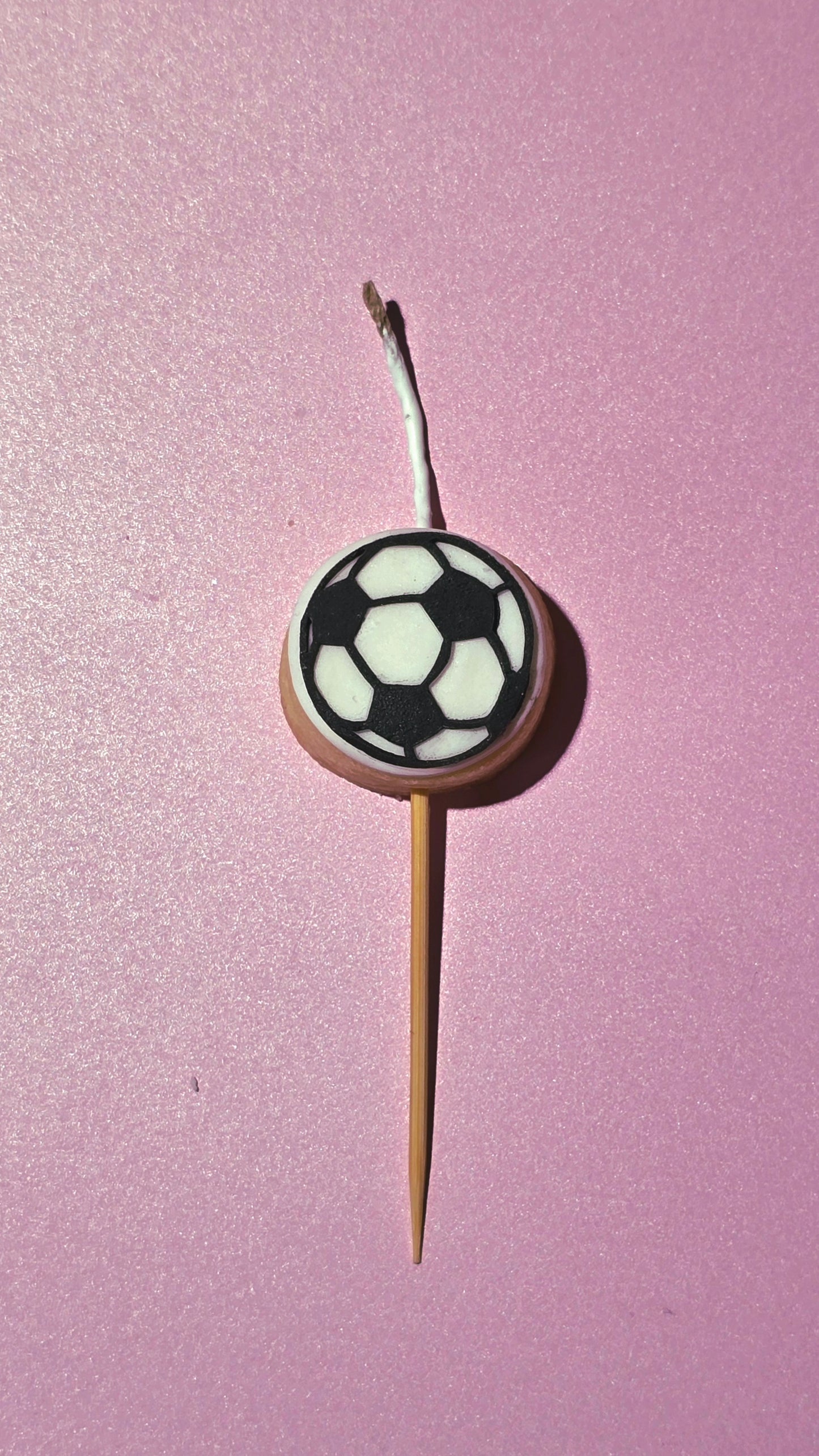 Soccer ball cookie candle on a stick against a pink background