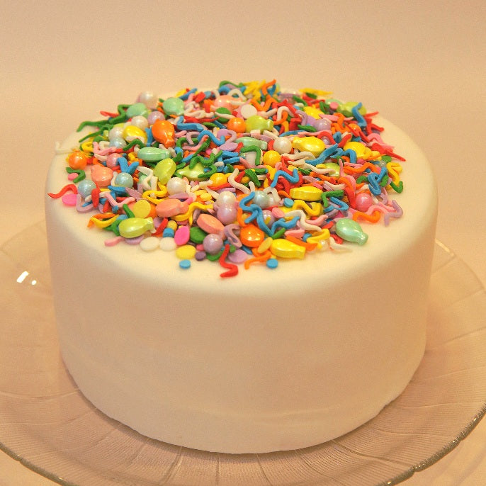 White cake with colorful balloon-shaped sprinkles on a beige background