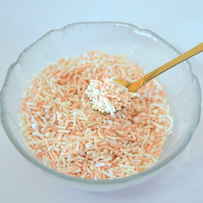 Clear glass bowl filled with pastel orange and yellow sprinkles on a light blue background
