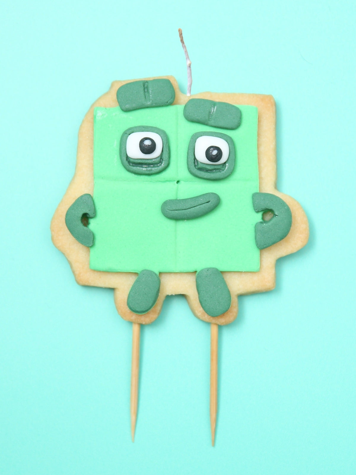 Cookie with green face and arms on a stick against a light blue background
