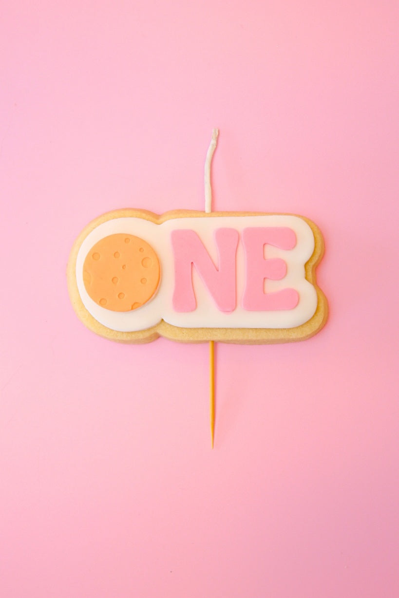 Candle shaped like the number 'ONE' on a pink background with orange planet 
